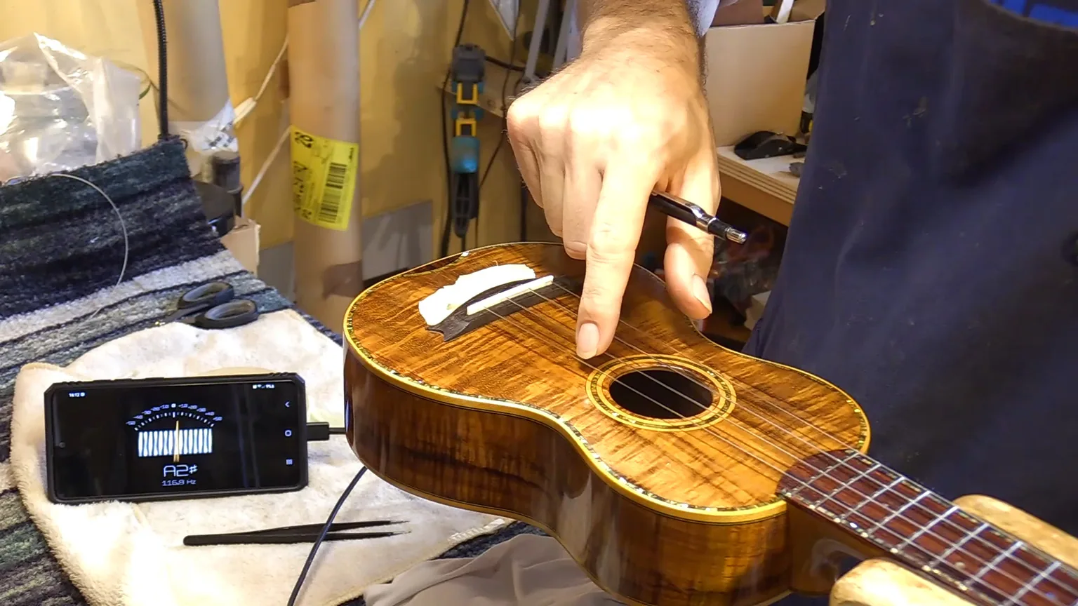 Ukulele in koa sul banco con accordatore elettronico e selletta provvisoria in fase di calibrazione